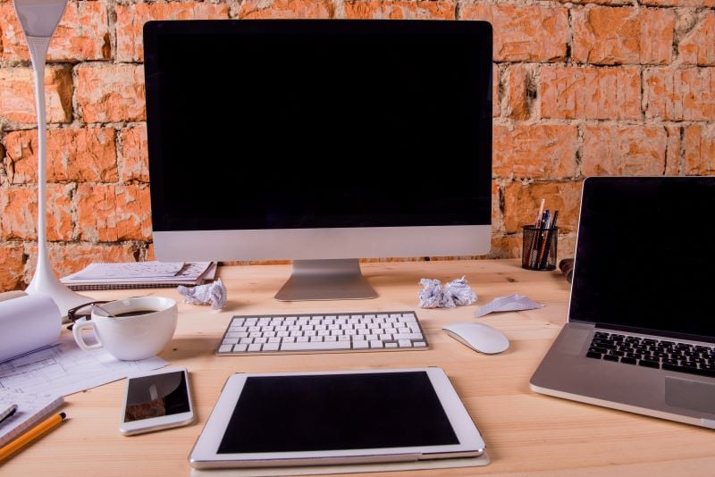 Desktop, laptop, tablet, keyboard, and phone sitting on a desk 